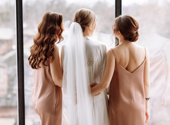 Morning of bride. Gorgeous bride with best bridesmaids are having fun in hotel room near the large window. Sexy bridesmaids in exciting negligee. Wedding morning details. back view.