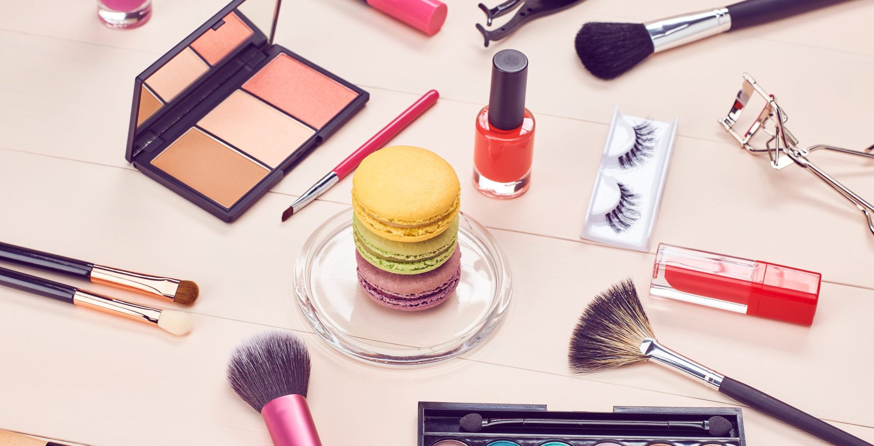 Still life, fashion woman essentials cosmetics. Beauty makeup accessories. Macarons french dessert. Lipstick, brushes, eyeshadow, false eyelashes, mascara.Unusual creative set. Vanilla wood background